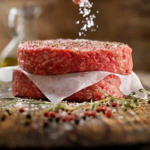 Raw meat patties with seasoning being added.