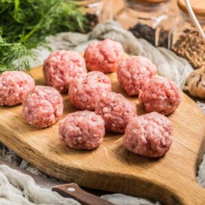 Raw meatballs on a wooden cutting board.