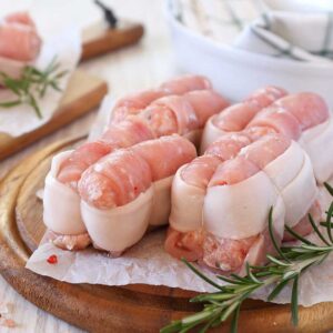 Raw meat wrapped in bacon on a cutting board.