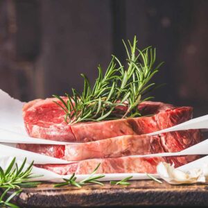 Raw meat with rosemary garnish on parchment.