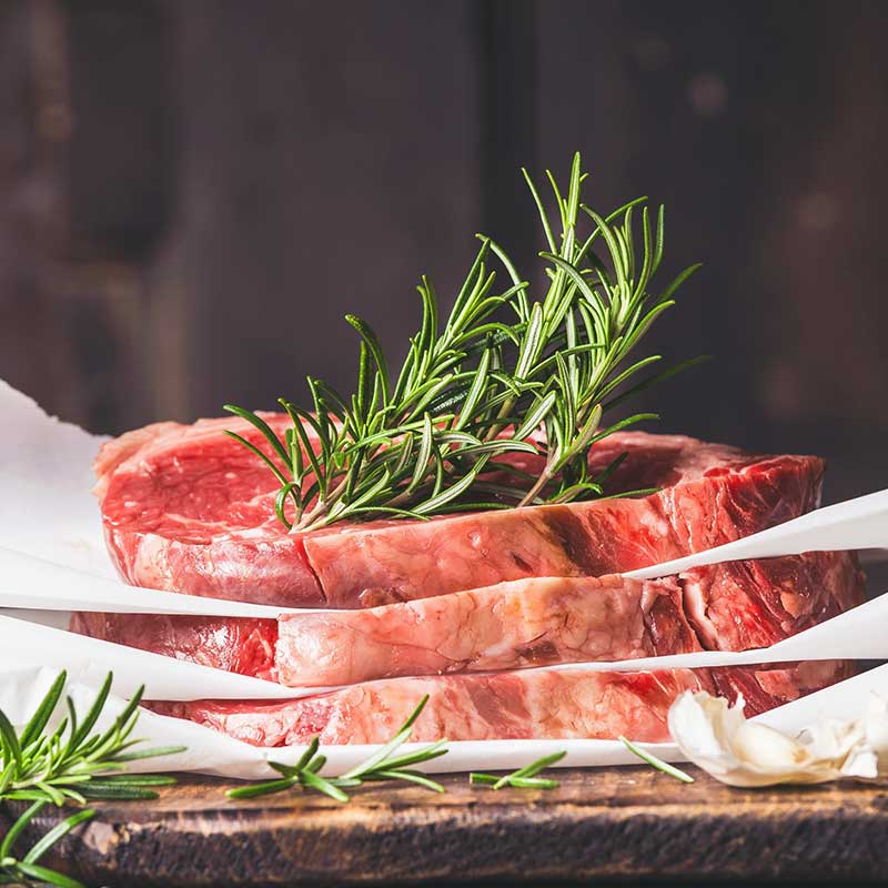 Raw meat with rosemary garnish on parchment.