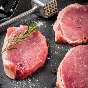 Raw pork chops with seasoning and herbs.